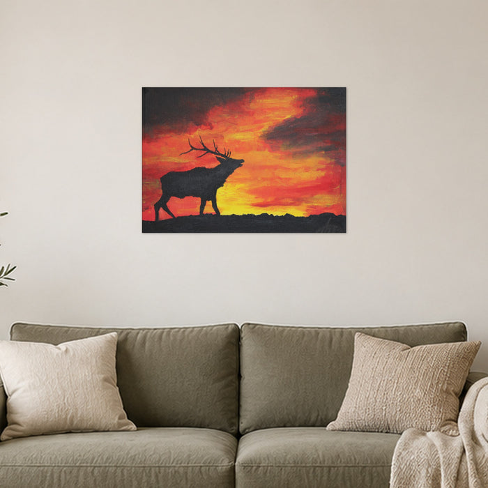 Where the sun becomes a beast art poster by Artis Berkmanis, a dark stag silhouette against a burning orange sunset sky. Unframed matte print shown at 70 x 50 cm above a sofa in a Scandinavian living room.