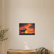 Where the sun becomes a beast art poster by Artis Berkmanis, a dark stag silhouette against a burning orange sunset sky. Unframed matte print shown at 40 x 30 cm in a Scandinavian hallway.